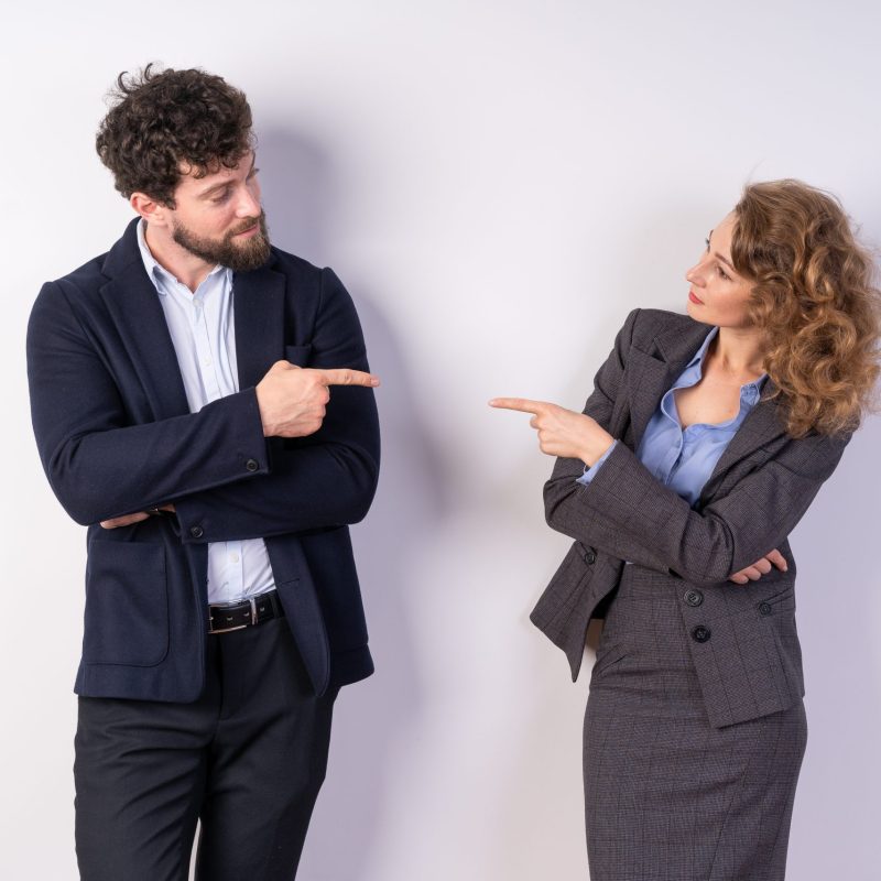 Man and woman standing side by side, pointing fingers at each other, business