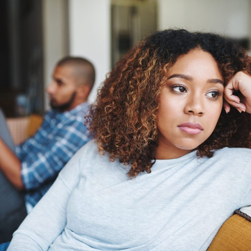 Unhappy couple and sad woman upset after argument or conflict with her man on home sofa. Angry girlfriend or female thinking about disagreement or ignoring partner, tired of relationship problems